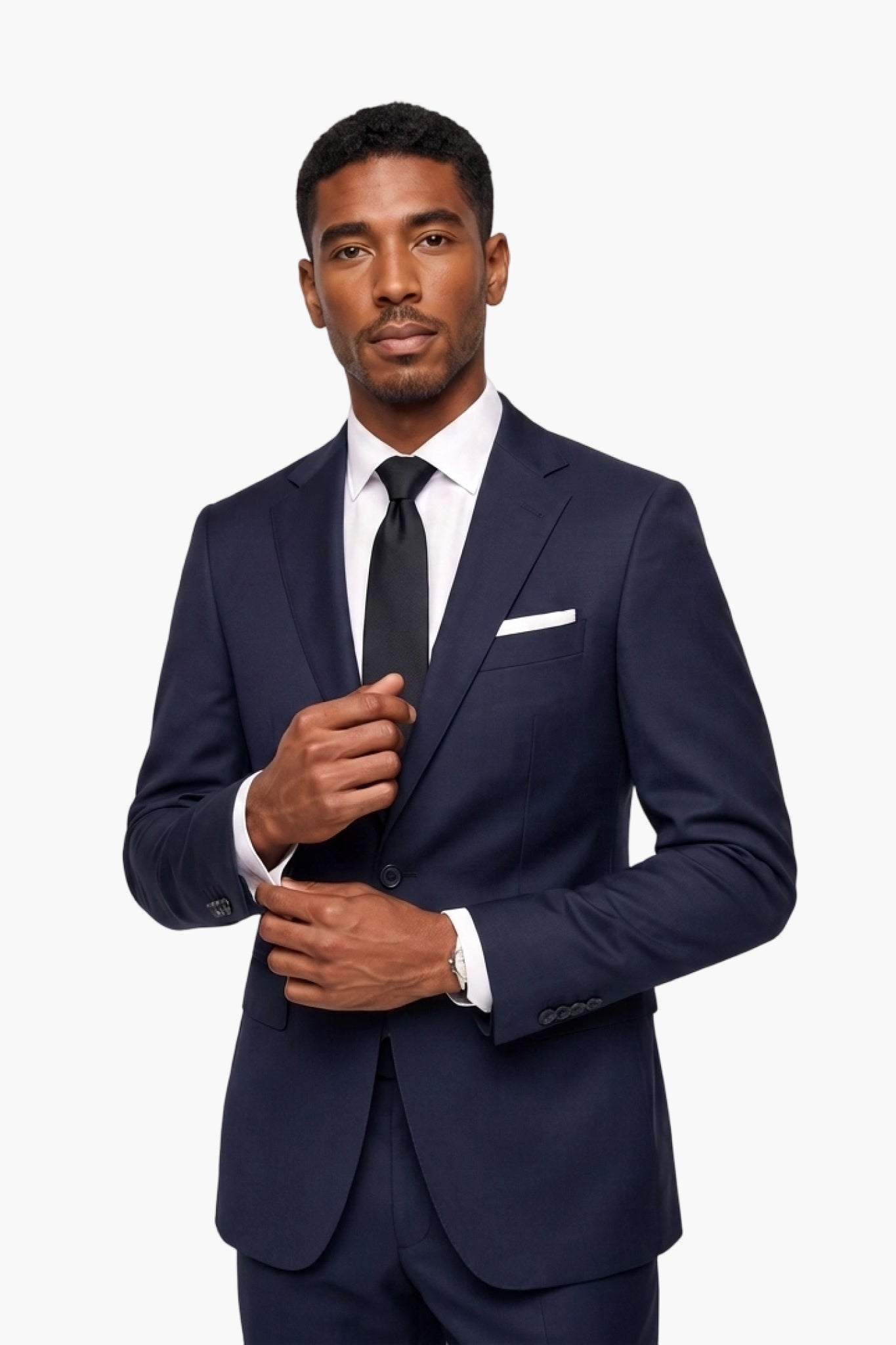 A man wearing a navy blue wool  notch-lapel suit, white dress shirt, black tie, and white pocket square, standing against a light gray studio background.