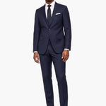 A man modeling a navy blue wool two-piece suit with a white dress shirt, black tie, and white pocket square, standing against a plain white background.