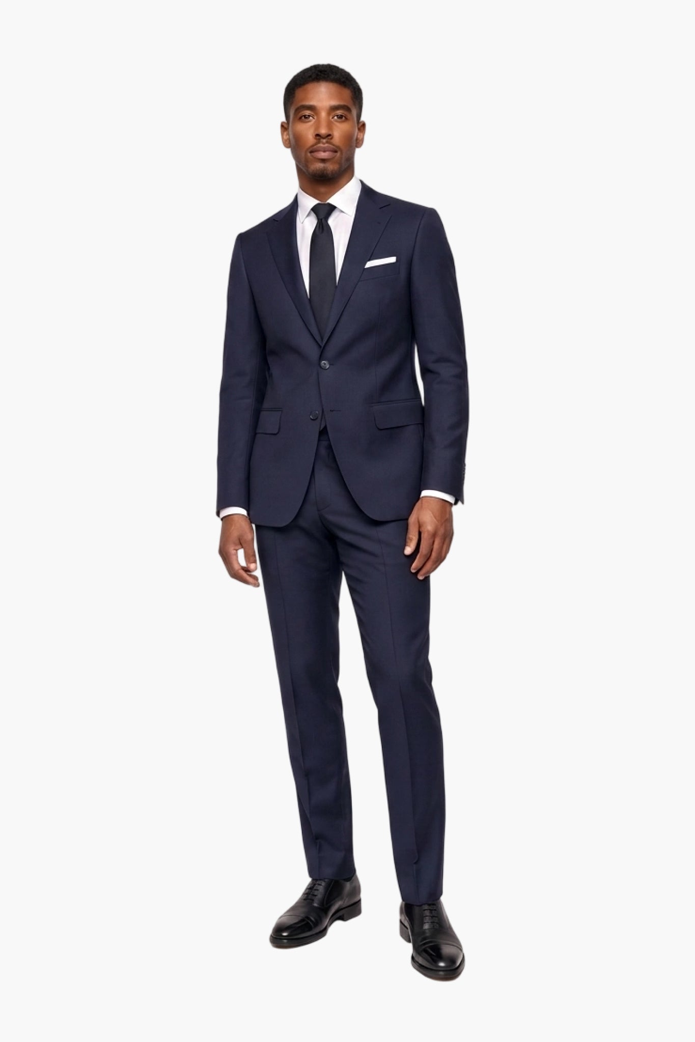 A man modeling a navy blue wool two-piece suit with a white dress shirt, black tie, and white pocket square, standing against a plain white background.