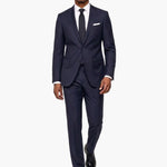 A man modeling a dark navy blue wool two-piece suit with a white dress shirt, a dark tie, and a white pocket square, set against a plain white background.