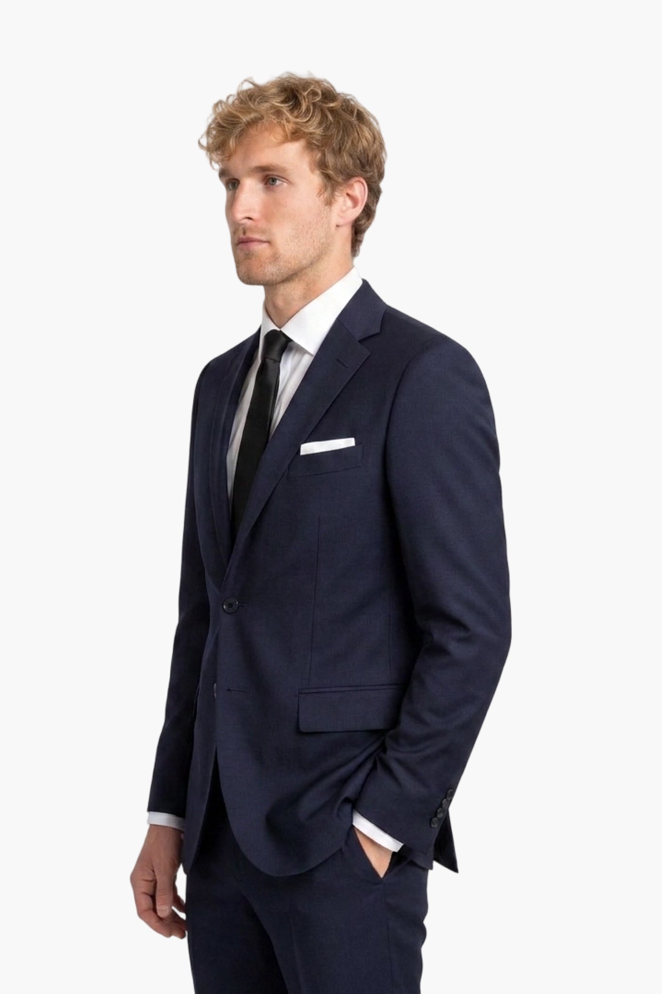 A man wearing a navy blue wool notch-lapel suit, white dress shirt, black tie, and a white pocket square, photographed against a plain light gray studio background.