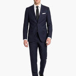 A man modeling a dark navy blue wool two-piece suit with a white dress shirt, black tie, and white pocket square, walking against a solid white background.
